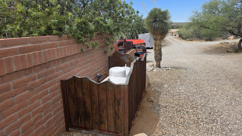 A desert-side HVAC installation in Tucson sits beside a red brick wall within a weathered wooden privacy enclosure. Gravel landscaping, a tall yucca plant, palo verde trees, and bright blue skies create a distinctly Southern Arizona settingwhere dependable cooling and routine HVAC service help keep homes comfortable through the heat.